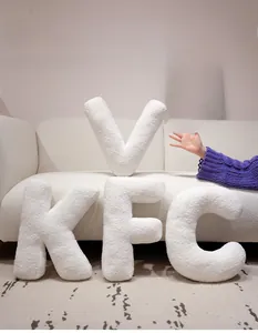 Soft white sherpa alphabet pillows showing K, F, C and V letters on a cozy sofa