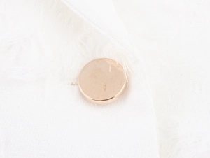 Dettaglio macro di un bottone dorato su tessuto bianco a frange di un cappotto largo
