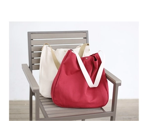 Detail of red and beige canvas tote bags with wide straps on a textured outdoor seat