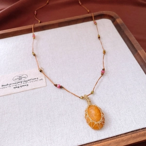 Macro detail of hand-woven wire wrapped orange gemstone pendant with vintage bead chain