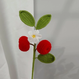 Macro shot of handmade crochet strawberry branch with white flowers and green leaves