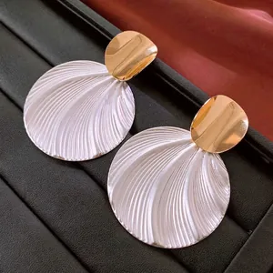 Golden irregular studs with large white round shell textured pendants on black display