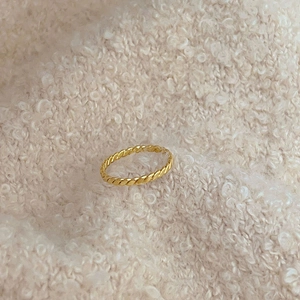 Close-up of golden braided rope texture ring on soft beige knitted fabric background