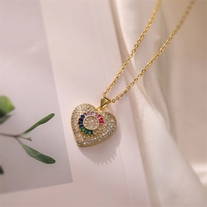 Close-up of gold heart pendant necklace featuring pavé zircon and a colorful gemstone center