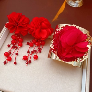 Détail des boucles d'oreilles fleurs rouges et du bracelet manchette doré à pompons