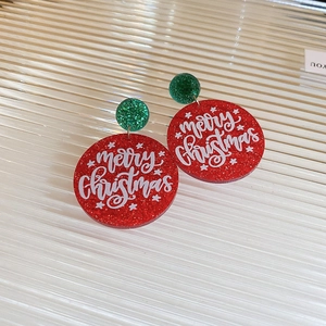 Macro shot of festive red and green acrylic earrings with Merry Christmas lettering
