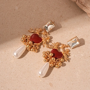Détail de boucles d'oreilles baroques cœur, cupidon doré et perle sur pierre