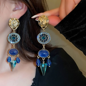 Nahaufnahme von Vintage-Goldohrringen mit blauen Kristallen und Porträtmünzen am Modell