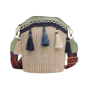 Detail of woven straw bucket bag with blue tassels and colorful geometric strap