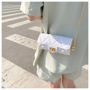 Close-up of white quilted cylinder bag with gold chain strap on a model shoulder