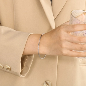 Minimalist silver open cuff bracelet with two small beads worn on a model wrist