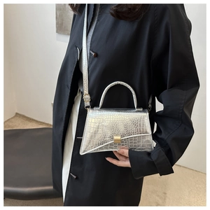 Detail shot of silver crocodile pattern handbag with golden metal lock and leather strap