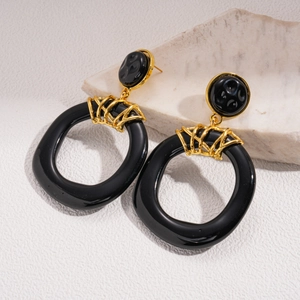 Detail view of black resin hoop earrings with gold metal frame on natural stone