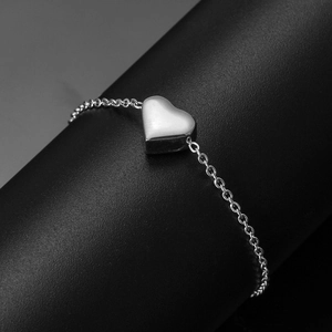 Macro shot of polished silver stainless steel heart pendant and fine chain bracelet
