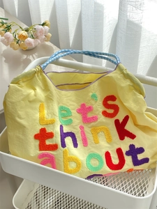 Close-up of a yellow canvas tote bag with colorful embroidery and blue checkered handles