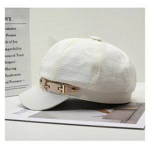 Detail of white newsboy cap featuring leather strap and gold metallic brand buckle