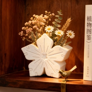 White ceramic flower-shaped vase with daisy floral arrangement in rustic wooden shelf
