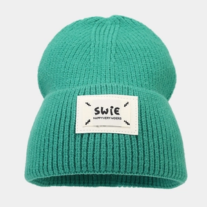Close-up of green knitted beanie showing chunky knit texture and SWIE logo patch detail