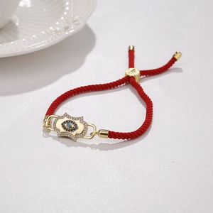 Close-up of red braided rope bracelet with gold Hamsa and blue Evil Eye charm