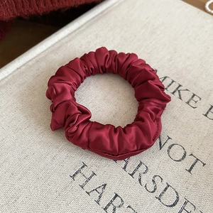 Detail of burgundy satin scrunchie with soft pleats on an elegant beige fabric background