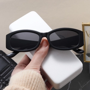 Detail view of black narrow rectangular sunglasses held against a beige fashion background