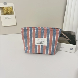 Dettaglio del beauty case in tela a righe rosa e blu con oggetti decorativi su sfondo bianco