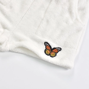 Détail du tissu en peluche blanc avec broderie papillon délicate et texture douce