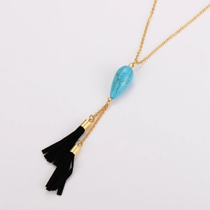 Vue détaillée du collier doré avec pendentif turquoise goutte et glands noirs sur blanc