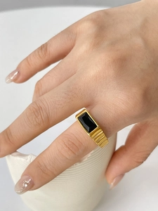 Close-up of gold ring with horizontal textures and a rectangular black gemstone