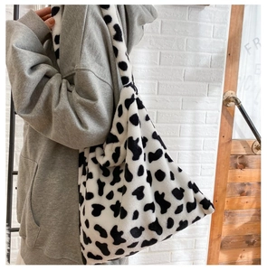 Detailed view of women's plush cow print tote bag worn with casual grey sweatshirt