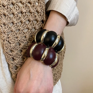 Close-up of retro acrylic resin bangles in matte black and burgundy with gold metal links