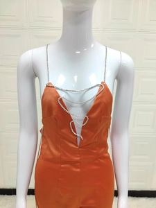 Detail of orange satin jumpsuit featuring sparkling rhinestone chains and deep V-neckline