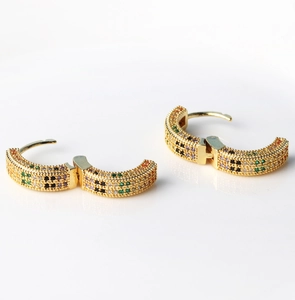 Detailed view of gold earrings with rows of colorful pave zircon stones on white reflective surface