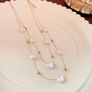 Detail shot of a double-layer gold chain with heart pearls on a vintage ceramic plate