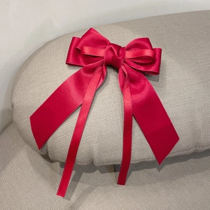 Elegant red satin bow hair clip with long ribbons shown on a gray textured background