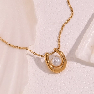 Macro view of 18K gold horseshoe pendant featuring a central round white pearl