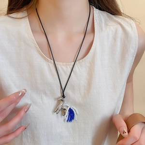 Macro shot of silver horse pendant with blue beaded tail on minimalist black necklace cord