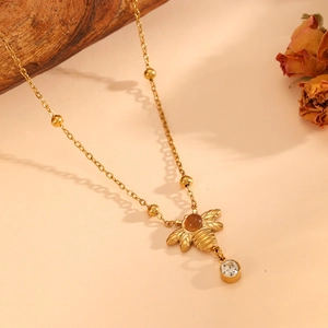 Gold bee pendant necklace with opal stone and crystal charm on warm natural background