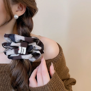 Close-up of a large striped fabric scrunchie with a vintage cloth tag on a low ponytail
