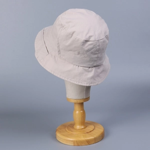 Minimalist beige cotton bucket hat for women on a wooden stand with a clean blue background