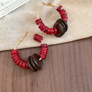 Détail de boucles d'oreilles rondes bohèmes avec perles de coco rouges et brunes sur or