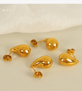 Macro detail of high-polish gold teardrop earrings on a clean cream background