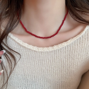 Close-up of a minimalist red glass beaded necklace worn over a beige knit top
