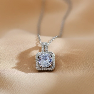Macro shot of a silver square halo pendant with a round zircon on champagne satin fabric