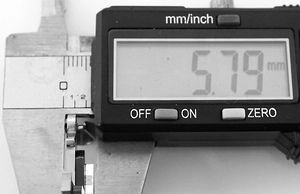 Close-up of digital caliper measuring a punk steel cross pendant detail at 5.79mm