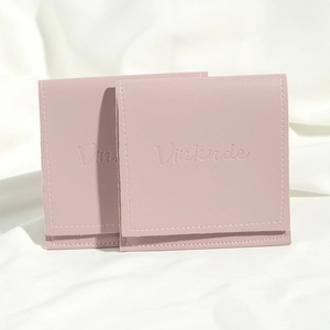 Detail of two pink PU leather drawstring pouches with embossed logo on soft white cloth