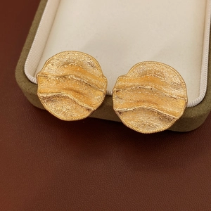 Détail de boucles d'oreilles rondes dorées avec texture martelée et bordure perlée sur velours