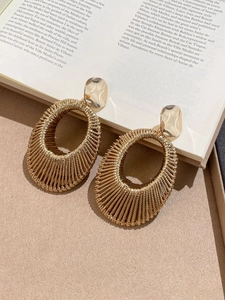 Detail shot of woven gold metal oval earrings resting on an artistic book background