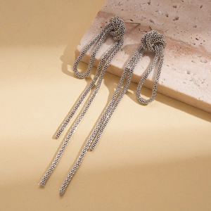 Detail view of silver knotted chain tassel earrings on a textured stone surface