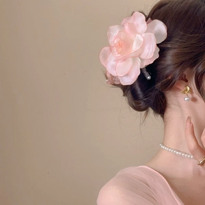 Detail view of a large soft pink fabric flower hair clip worn by a model in warm light